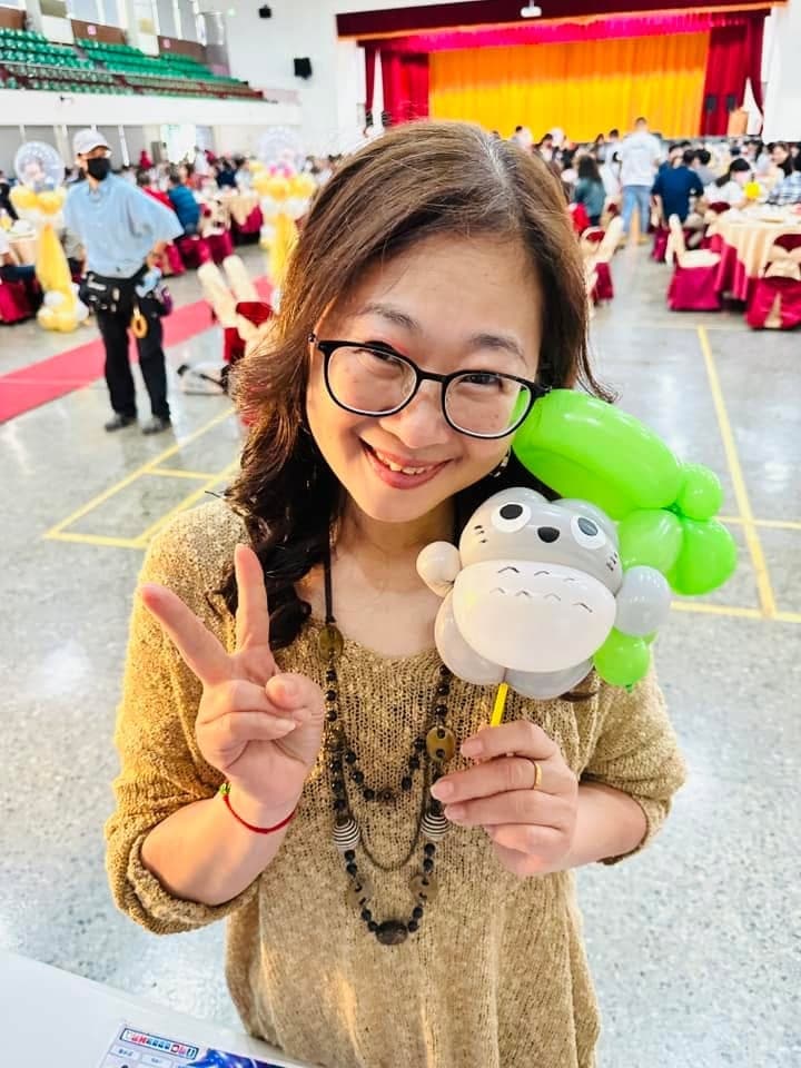 戴眼鏡的女賓客比 YA，手拿頭頂綠葉的灰色龍貓造型氣球