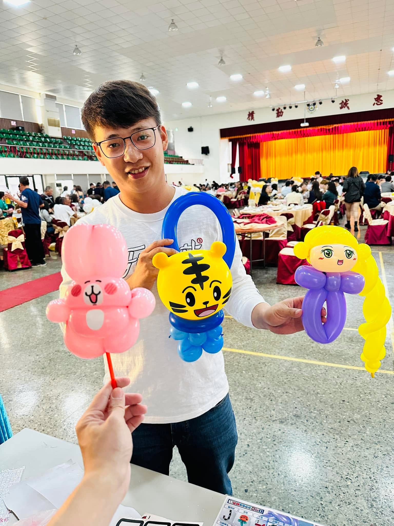 男賓客展示巧虎提把氣球、金色長辮公主手環，旁邊遞來粉紅兔子氣球