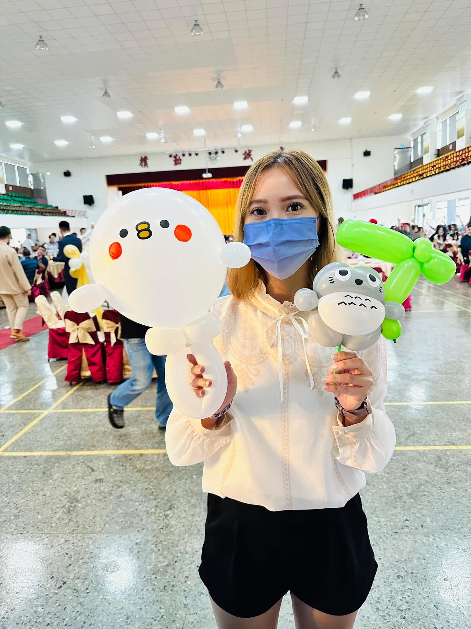 女賓客一手拿白色小雞氣球、一手拿灰色龍貓氣球，背景是流水席圓桌