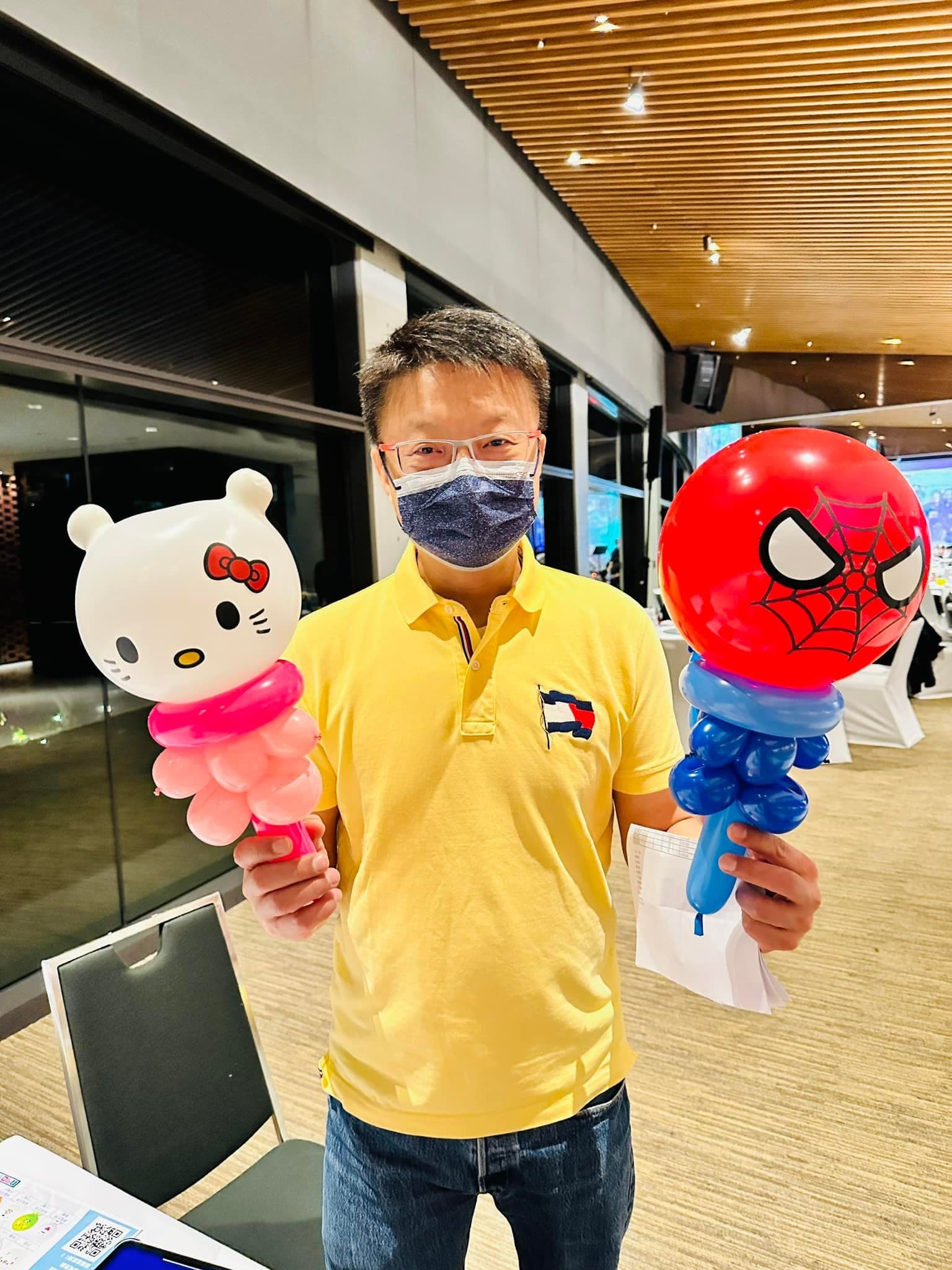 穿黃色 POLO 衫的男賓客一手拿 Hello Kitty、一手拿蜘蛛人造型氣球棒