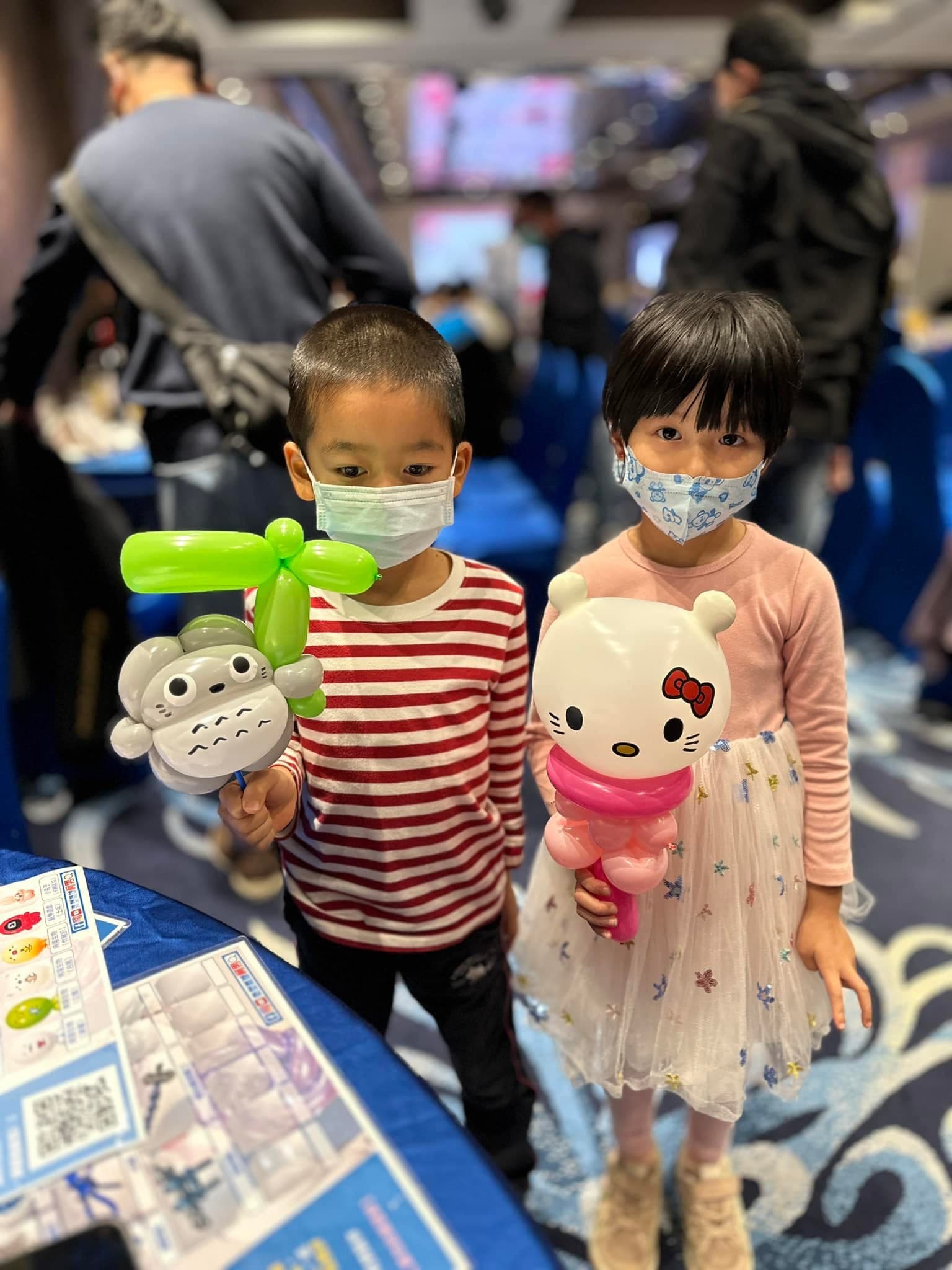 男孩拿龍貓氣球、女孩拿 Hello Kitty 氣球，站在尾牙會場
