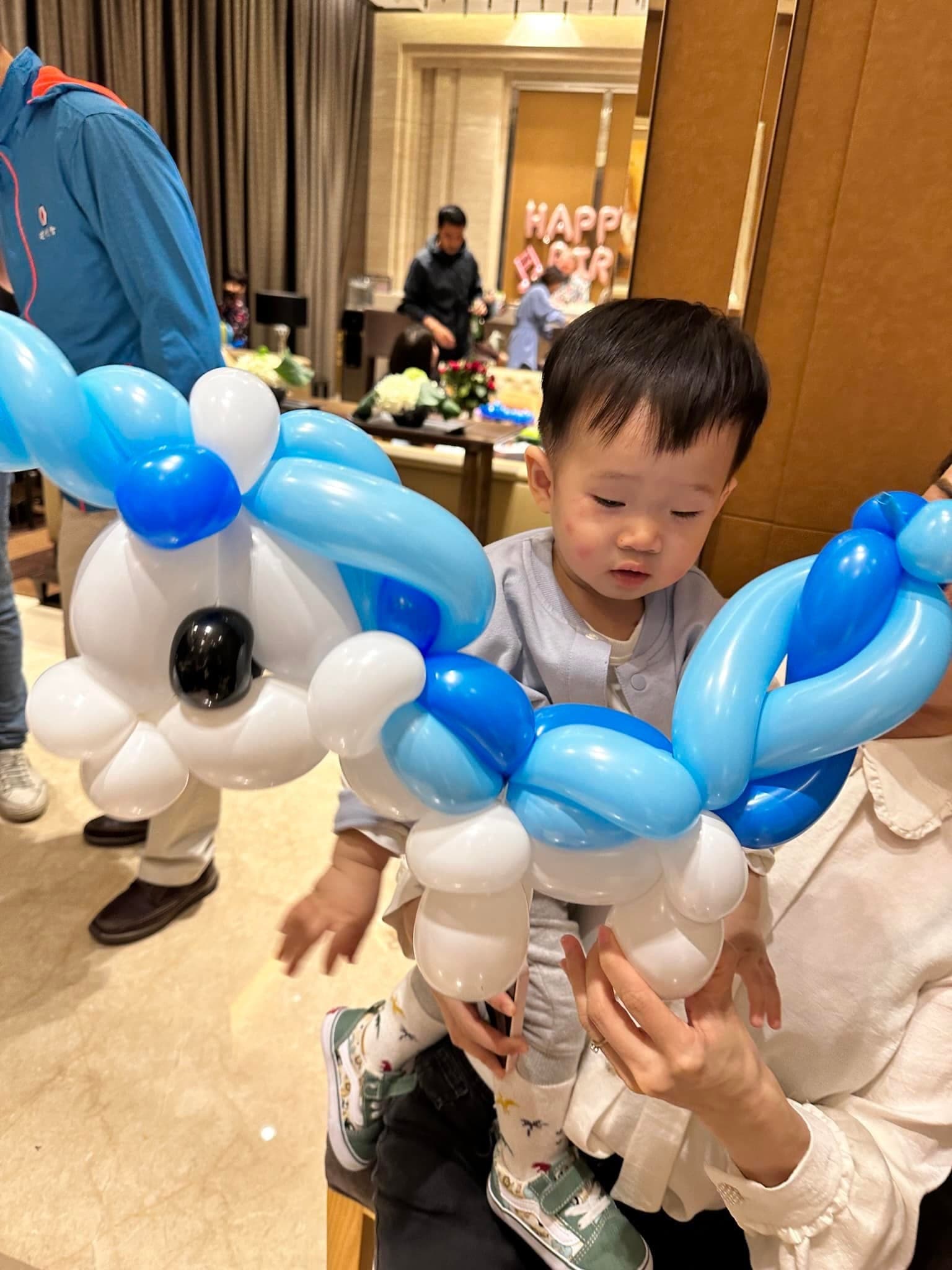 幼兒被大人抱著，面前是藍白色、黑鼻子的大型造型氣球