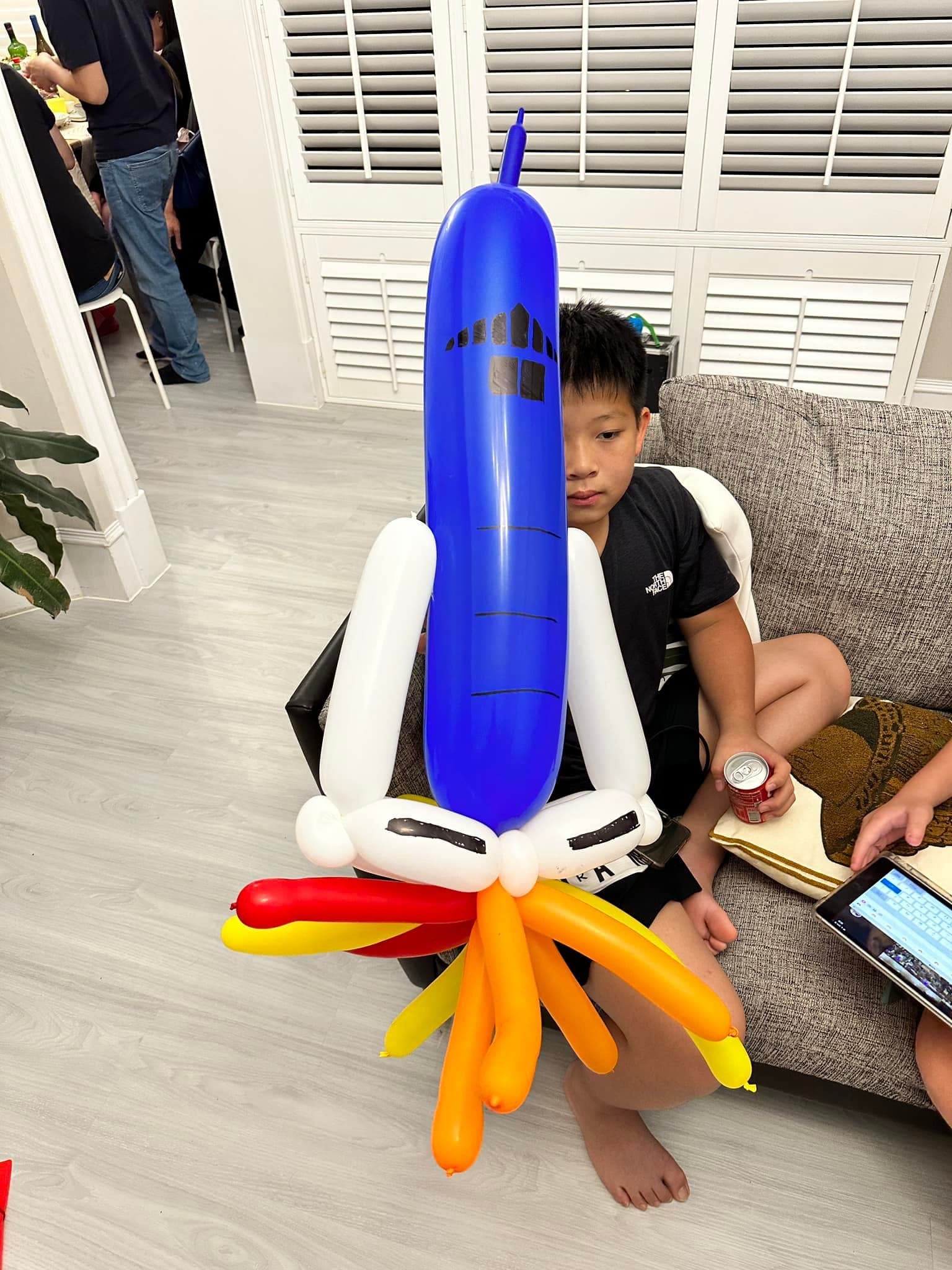 男孩坐在沙發上，身前是藍色火箭造型氣球