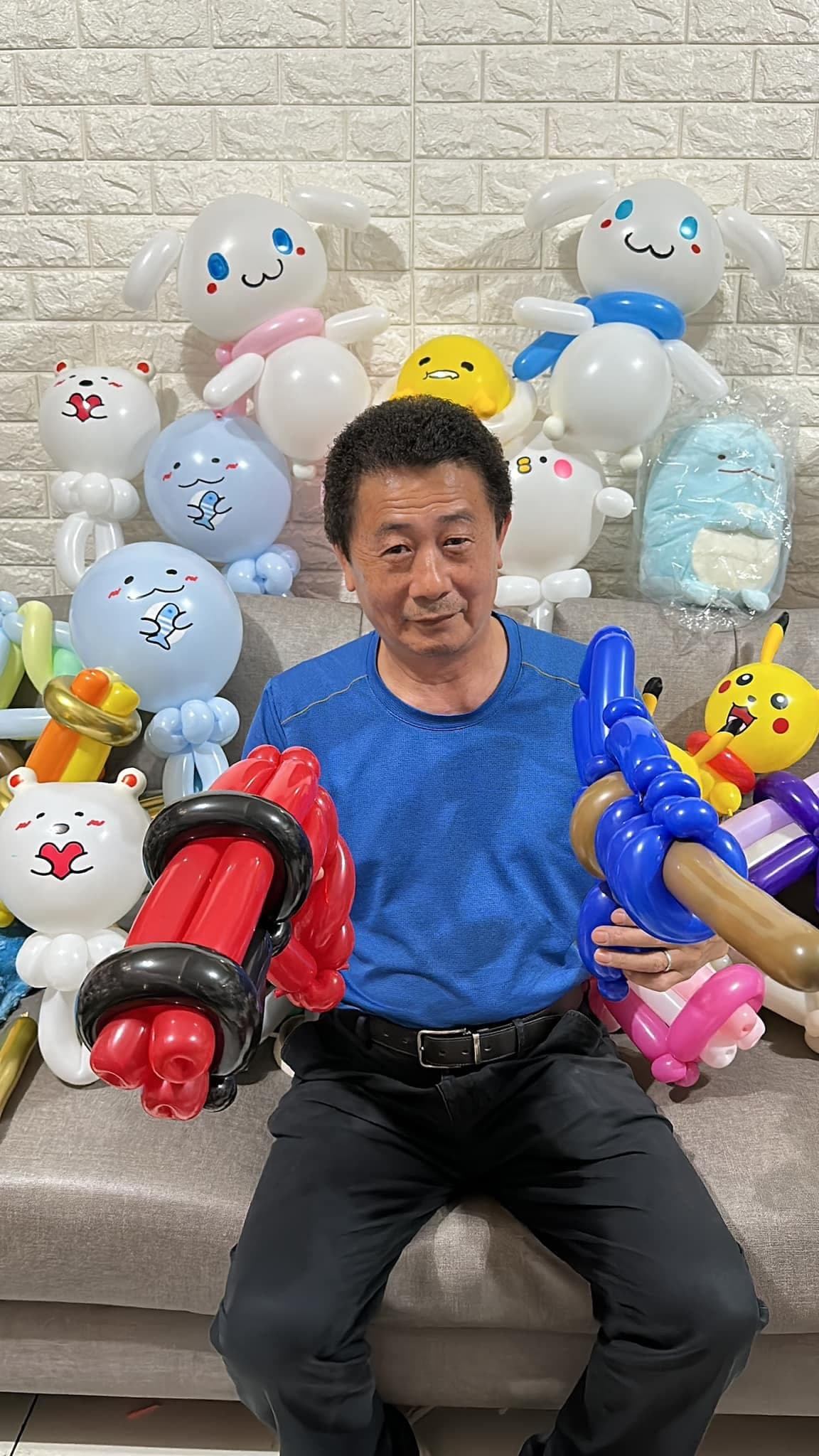 柯爹坐在造型氣球堆中，雙手拿著紅色與藍色氣球槍