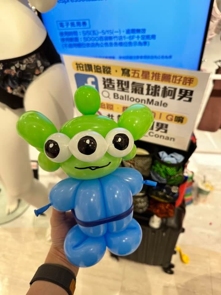 綠色三眼怪造型氣球，身穿藍色連身衣