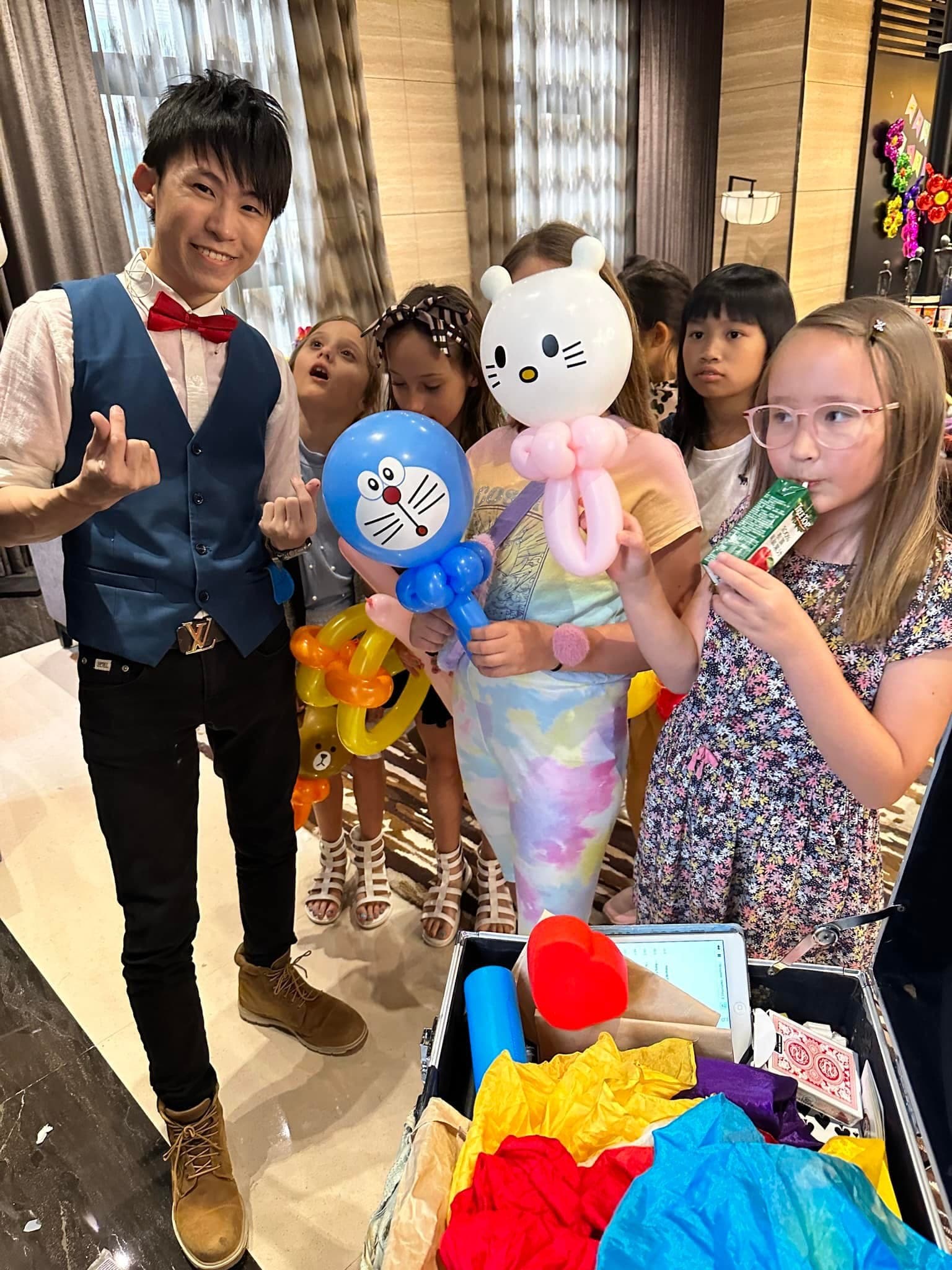 女孩們拿著哆啦A夢和 Hello Kitty 造型氣球，站在柯男旁邊