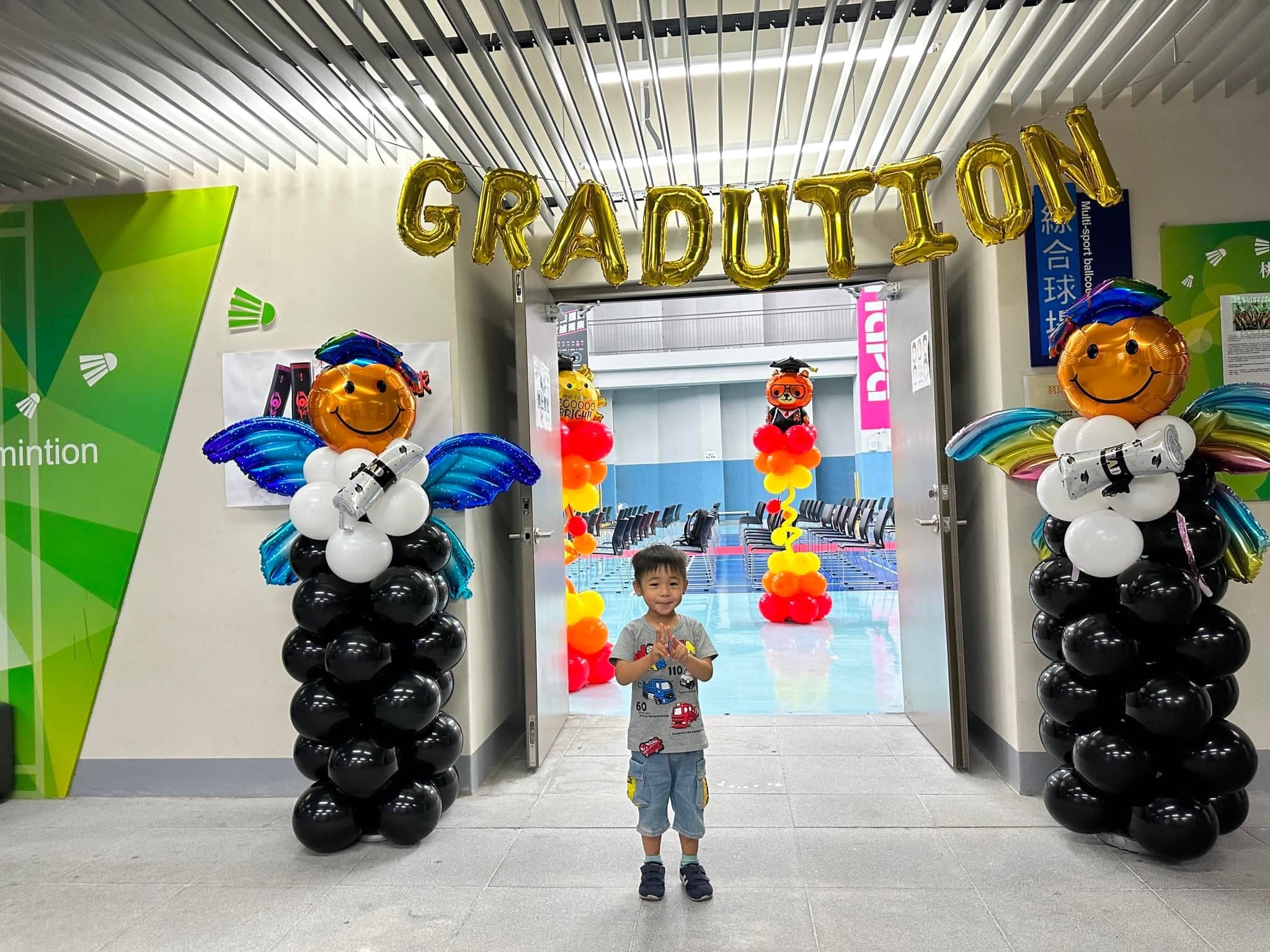 球場入口上方掛著金色 GRADUATION 字母，兩側是戴學士帽、有翅膀的畢業天使氣球柱