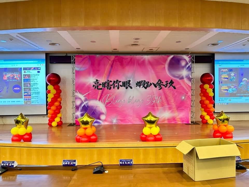 粉紅背板舞台兩側立著紅橘黃氣球柱，台前是金色星星氣球座