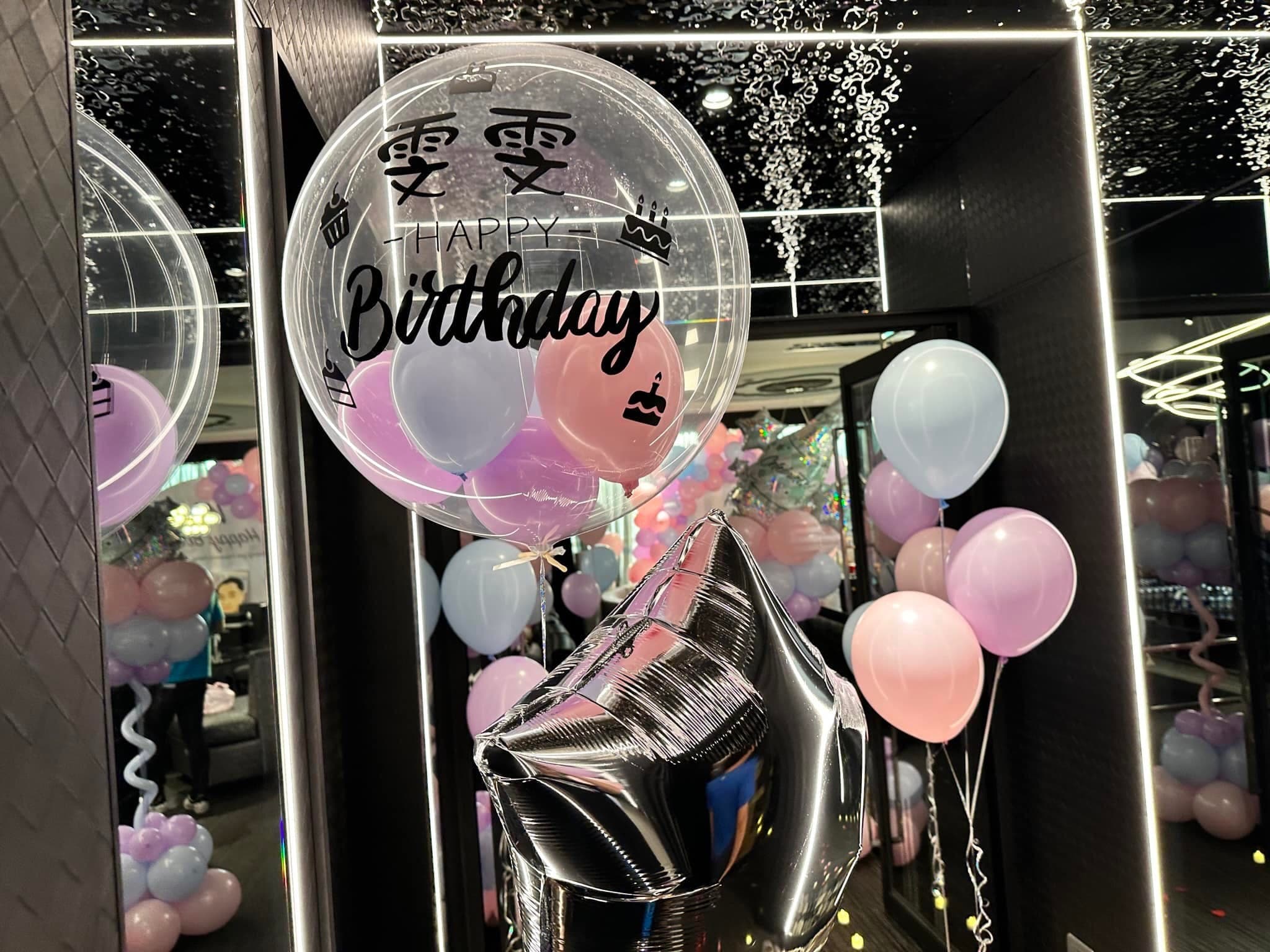 寫著壽星名字與 Happy Birthday 的透明波波球，搭配銀色星星和粉紫氣球束，倒映在包廂鏡牆上