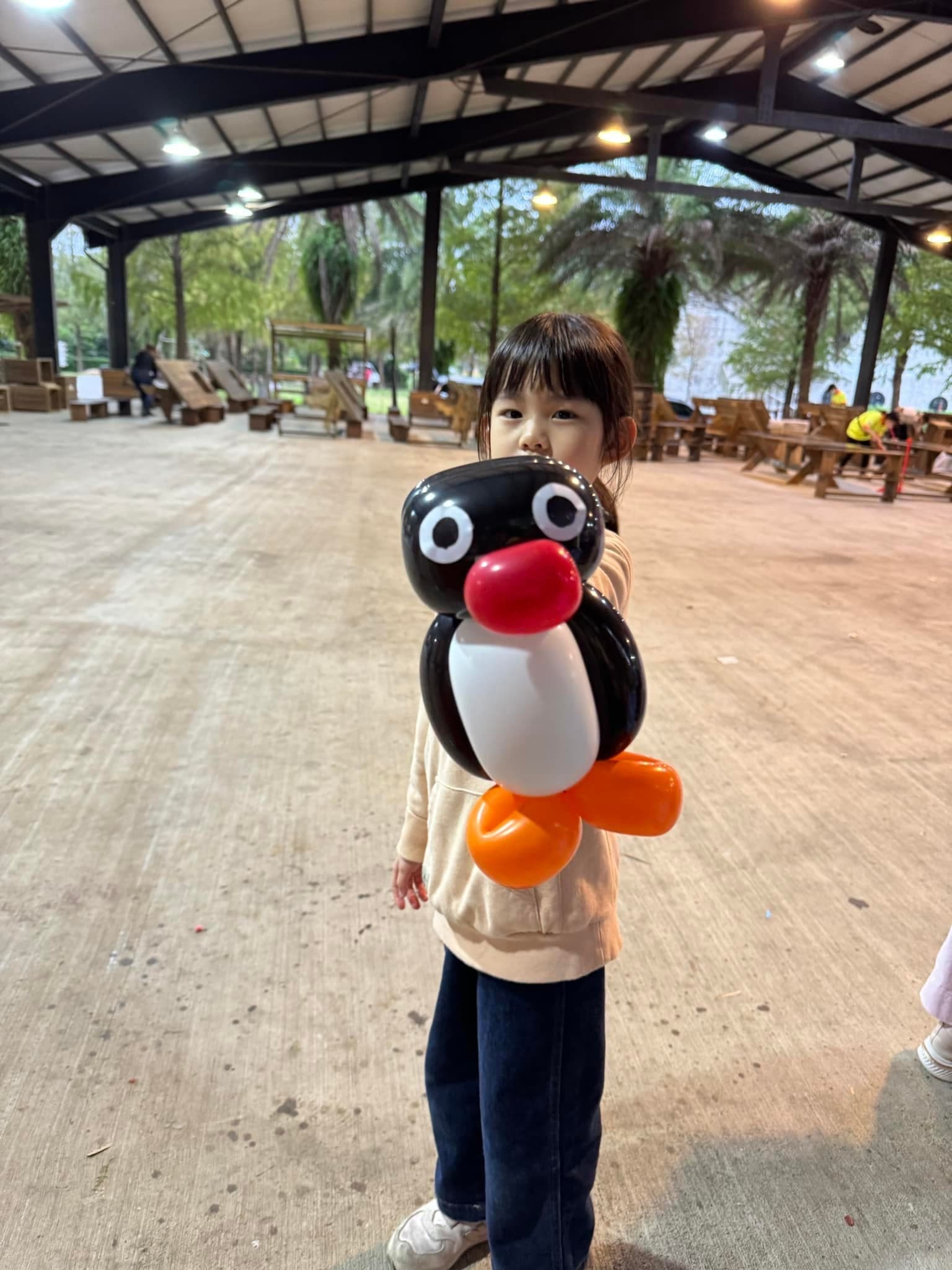 小女孩在涼亭裡舉起黑白紅嘴的企鵝家族 Pingu 氣球