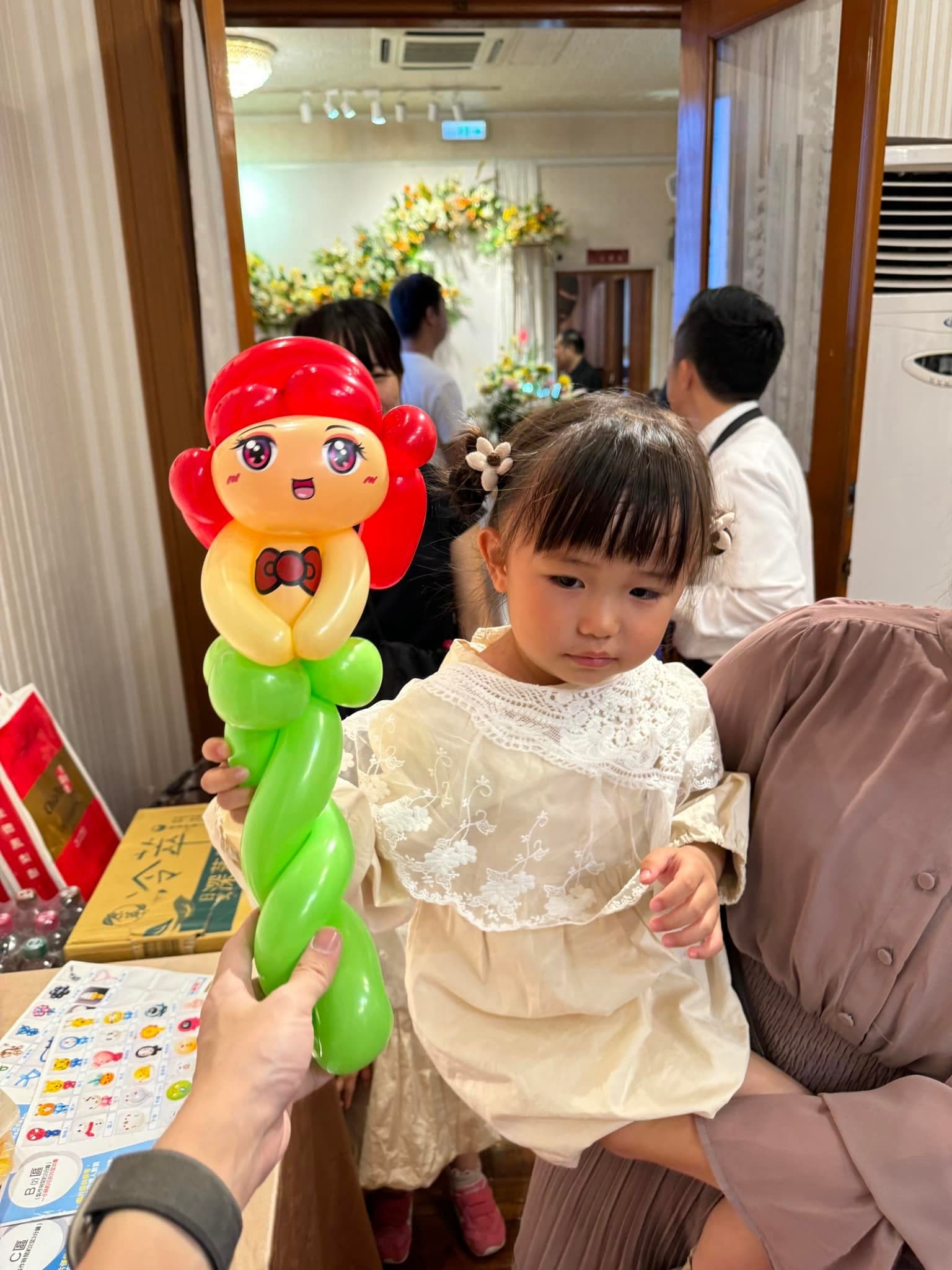 穿白色蕾絲洋裝的小女孩看著紅髮公主造型氣球棒