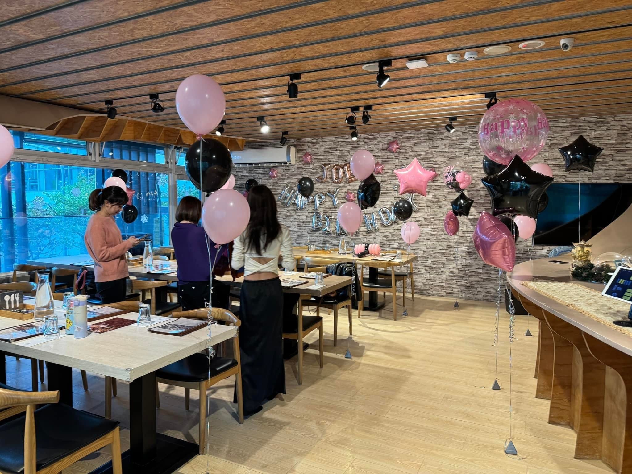 粉色黑色空飄氣球立在餐桌間，幾位女士正在整理派對餐桌