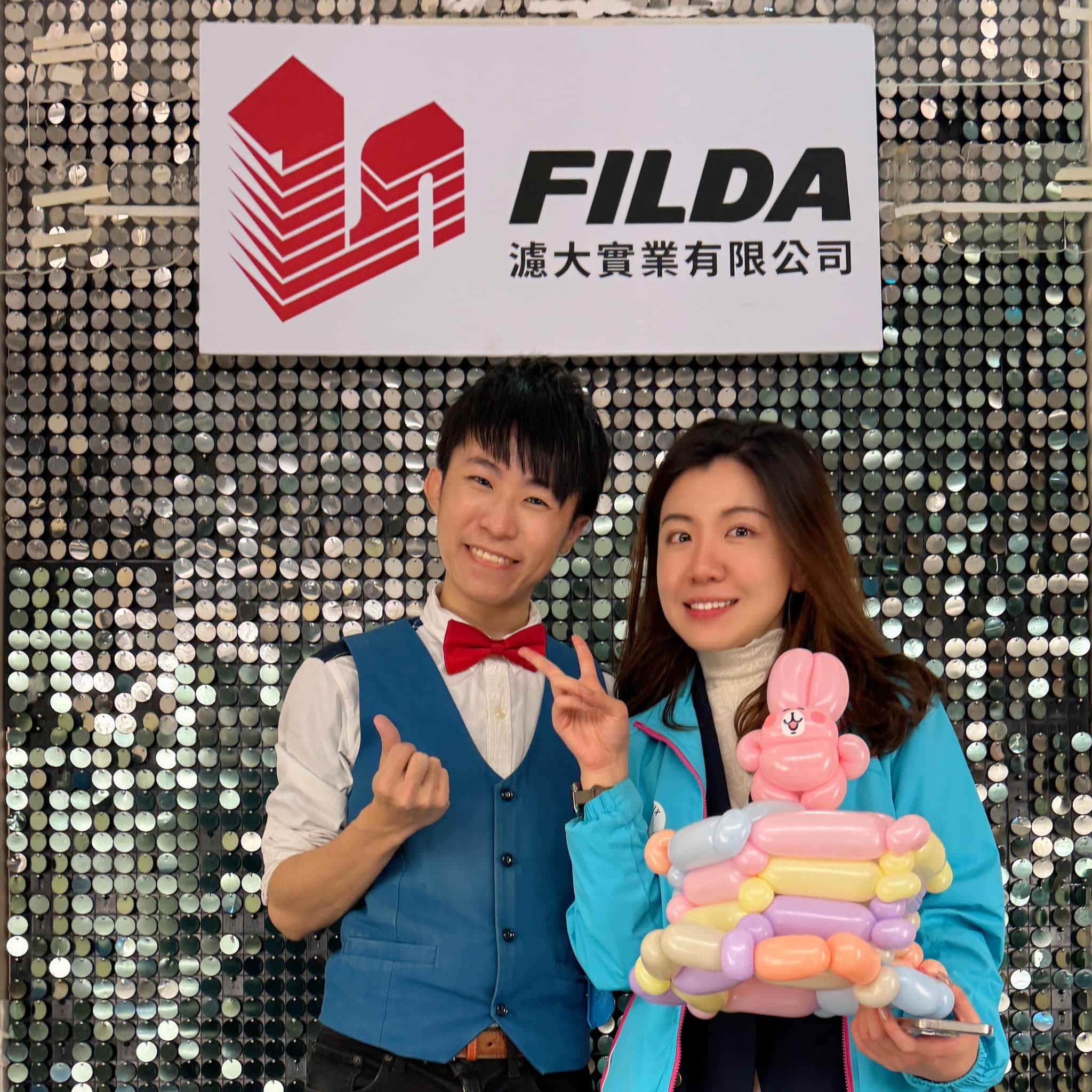 柯男和女賓客在亮片公司背板前合照，女賓客抱著疊在彩色氣球上的粉紅兔子