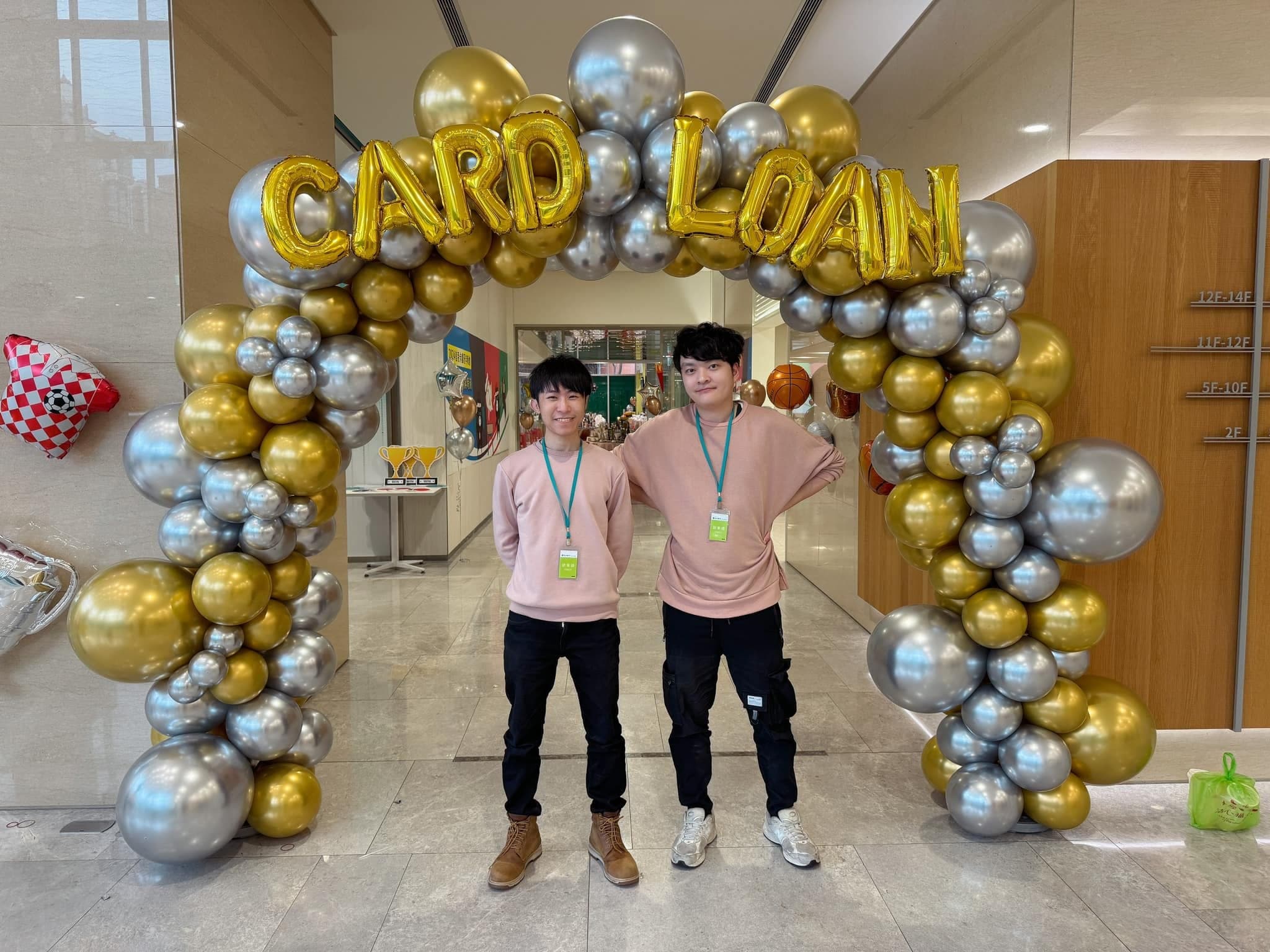 金銀鏡面氣球拱門上掛著 CARD LOAN 字母，柯男與夥伴站在下方