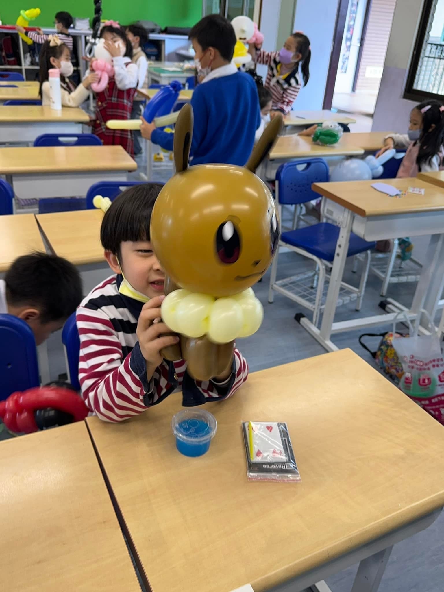 穿條紋上衣的學生坐在課桌前，抱著咖啡色伊布造型氣球