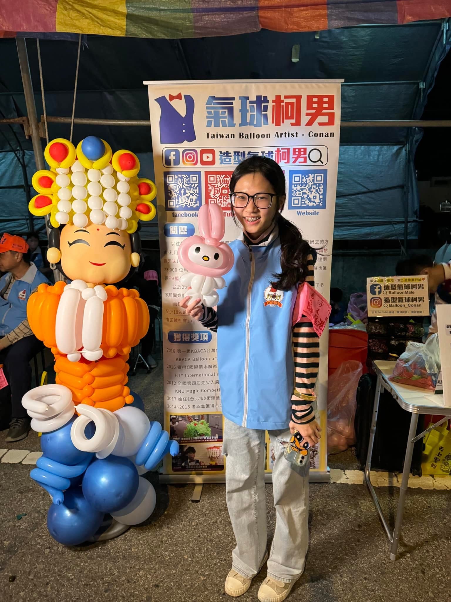 穿淺藍背心的少女拿著美樂蒂氣球站在媽祖氣球旁