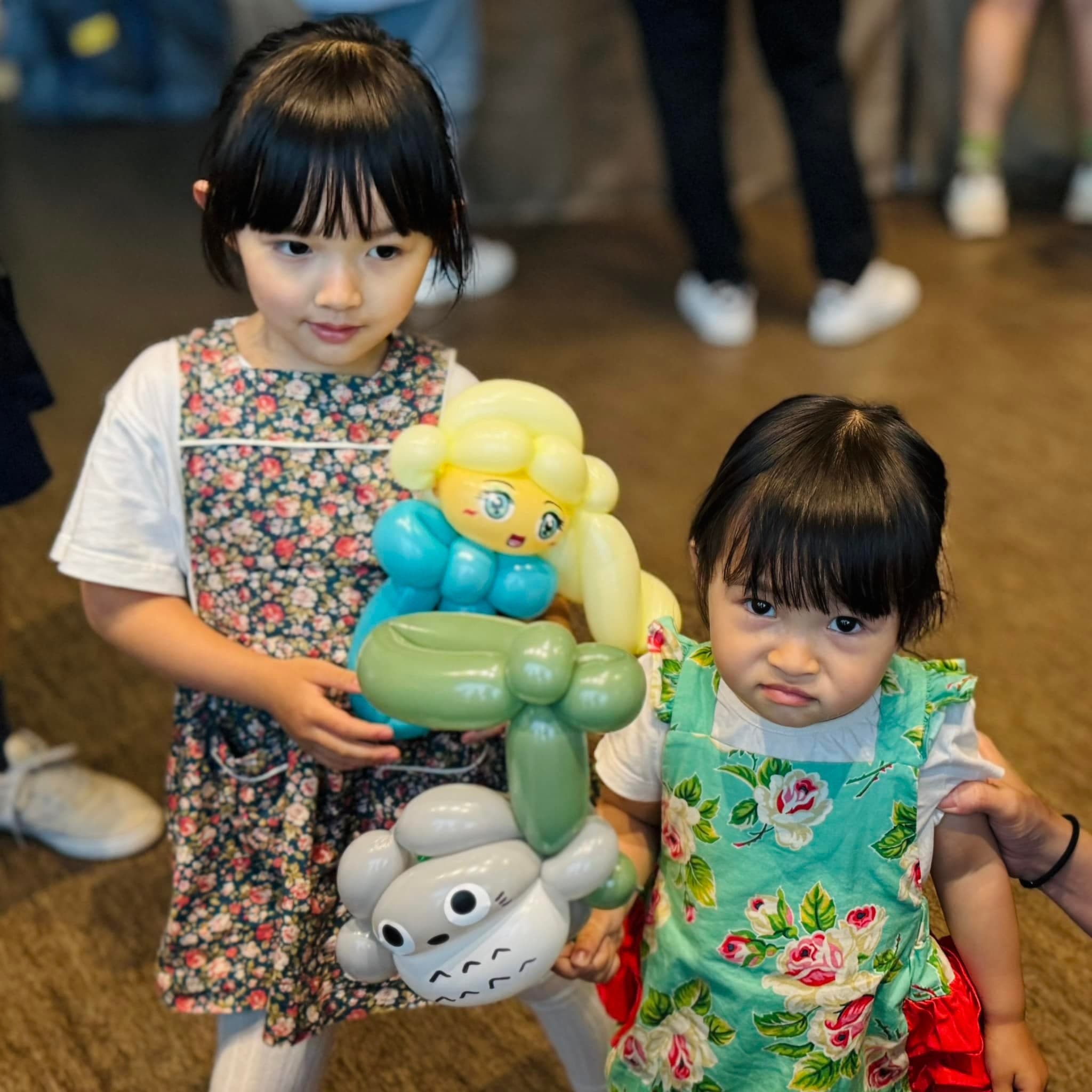 兩個小女孩分別抱著金髮藍裙公主與龍貓造型氣球