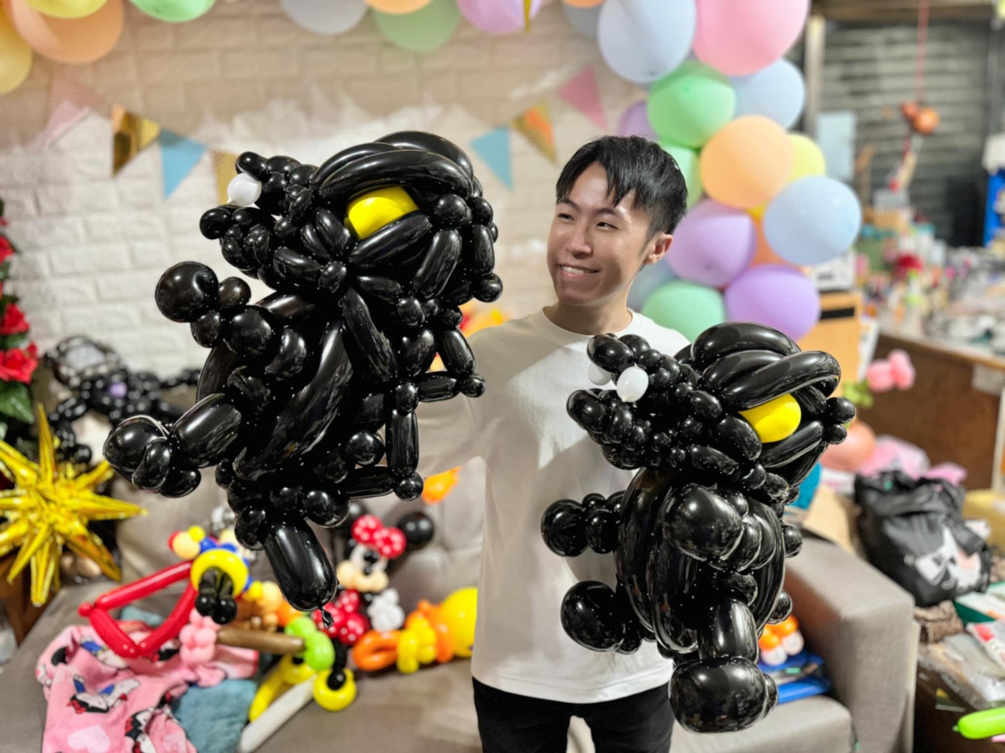 柯男在工作室裡雙手各拿一隻全黑黃眼的哥吉拉造型氣球
