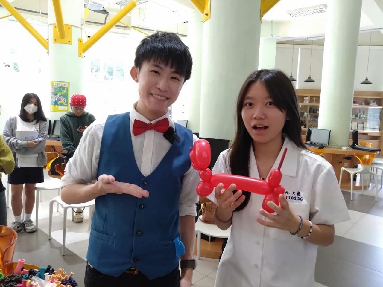 學妹拿著紅色臘腸狗造型氣球，柯男在旁比手勢介紹