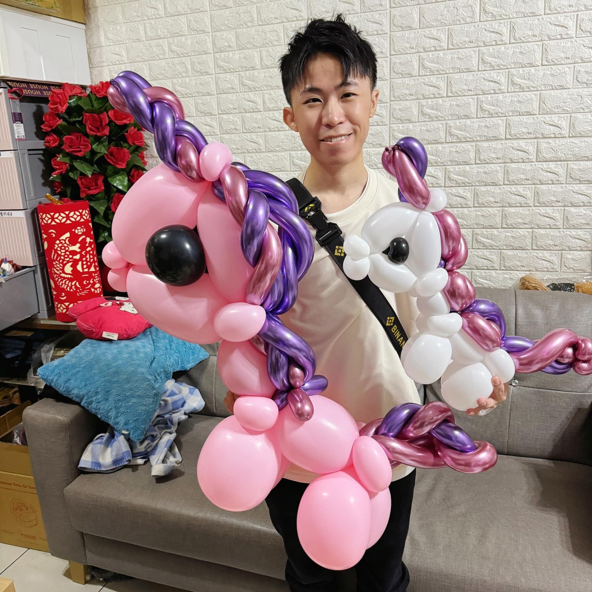 我在家裡客廳抱著兩隻獨角獸造型氣球，一隻粉紅色、一隻白色，鬃毛是紫色和玫瑰金的扭紋