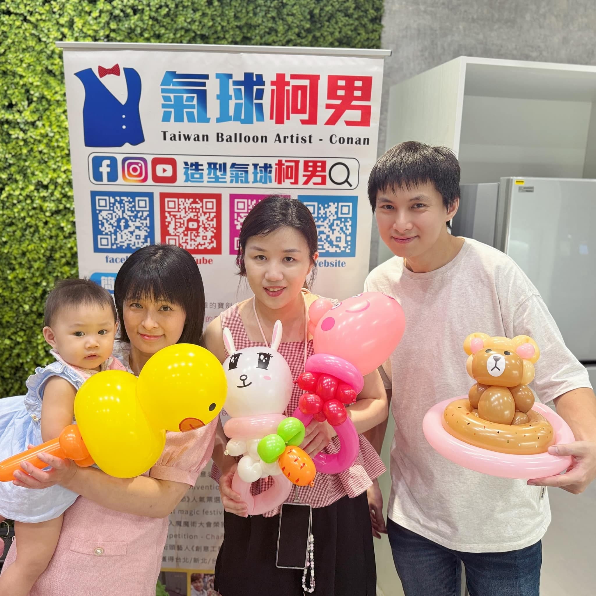 一家人在氣球柯男海報前合照，拿著黃色小鴨、白兔、粉紅角色與泳圈小熊氣球