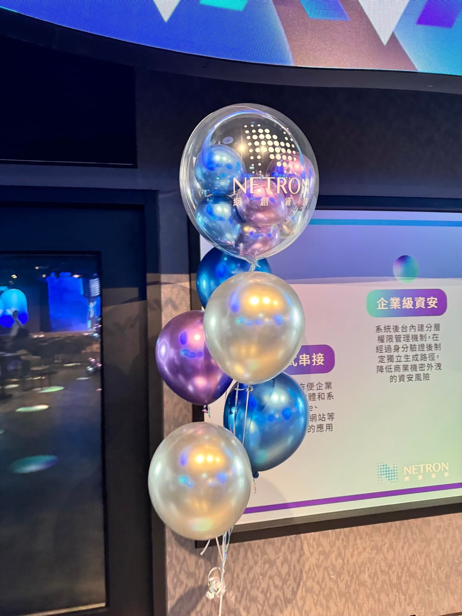 展示看板旁的波波球氣球束，銀色與藍紫色金屬氣球由上往下排列