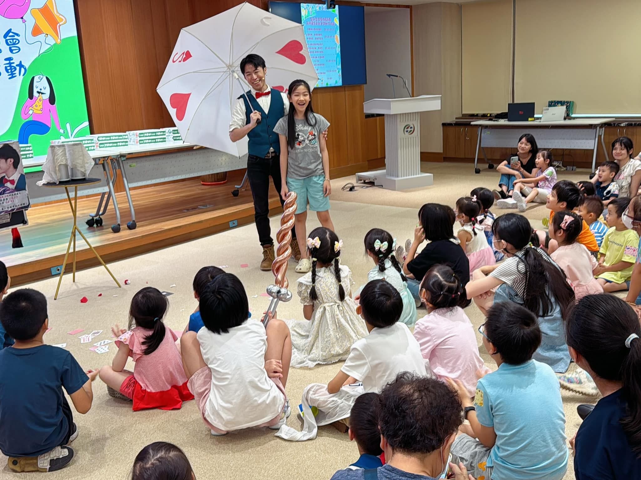柯男撐開愛心圖案魔術雨傘，上台的小女孩在一旁幫忙