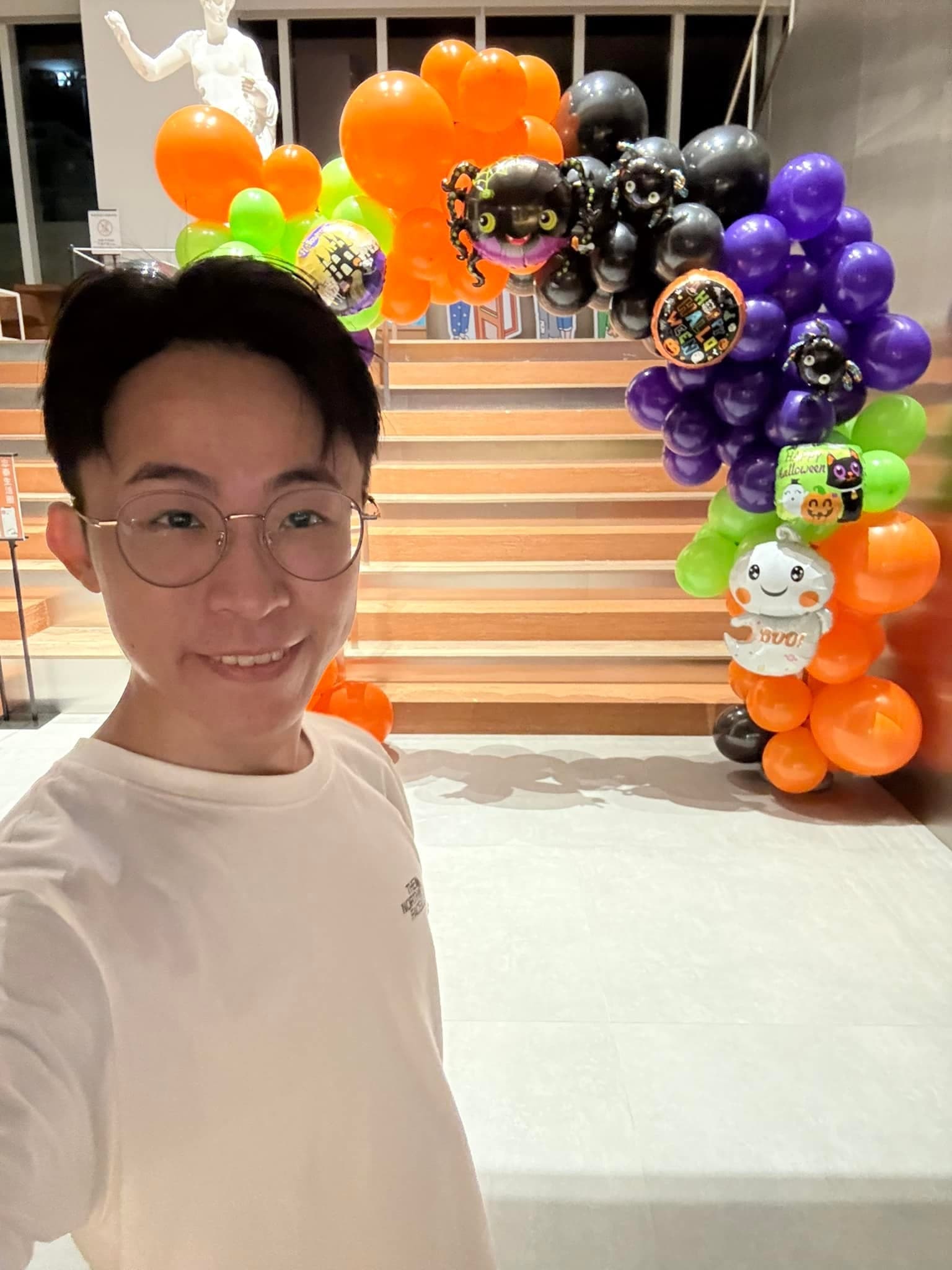 柯男戴眼鏡在商場內自拍，身後是剛完成的萬聖節氣球拱門