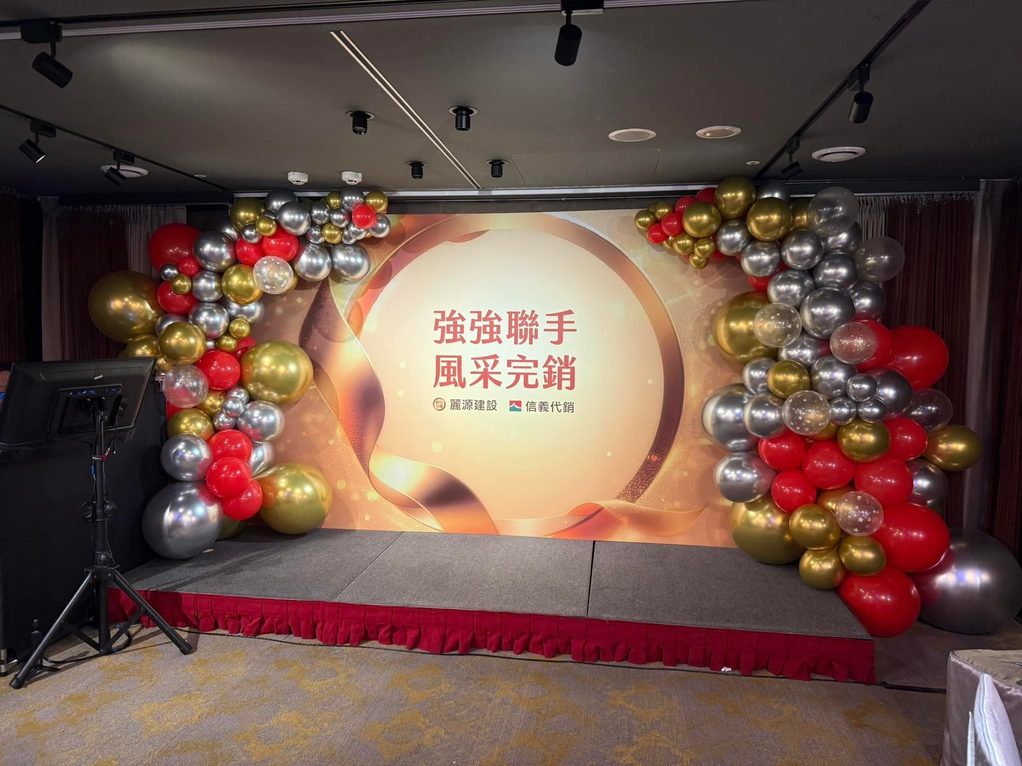 燈光調暗後的舞台全景，氣球串框住強強聯手背板