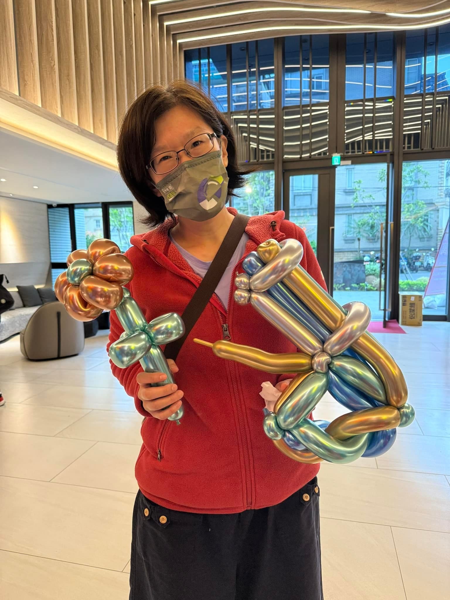 建案大廳裡一位女士拿著金屬色花朵氣球和金屬色劍形氣球
