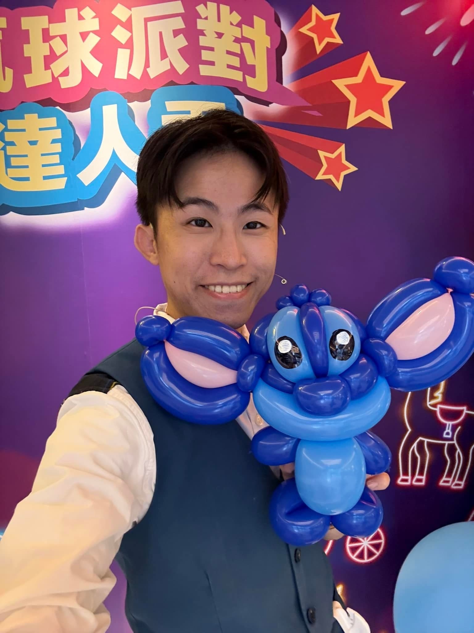 柯男在活動背板前自拍，肩上扛著藍色史迪奇造型氣球
