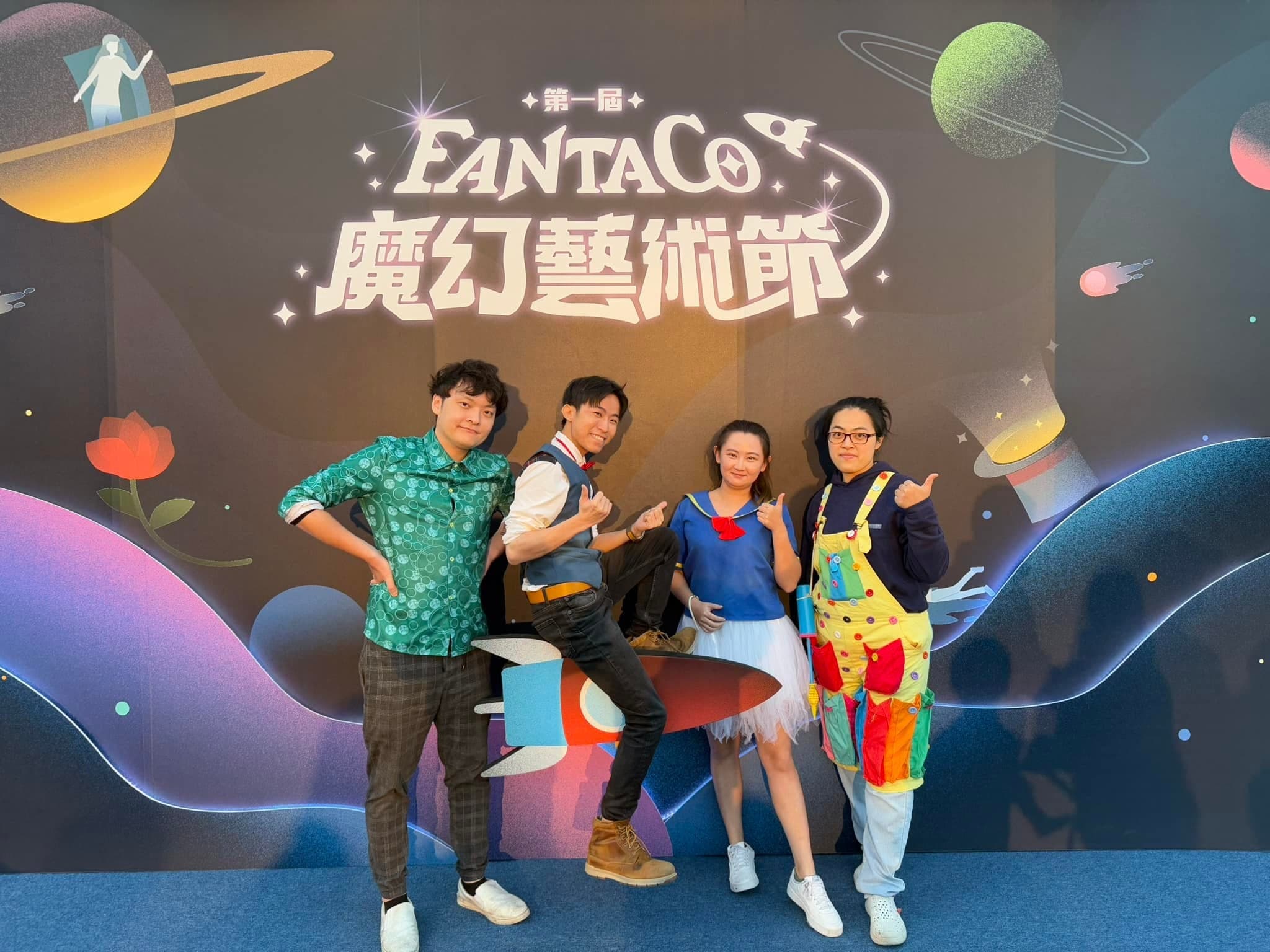 柯男和三位夥伴在第一屆 FANTACO 魔幻藝術節主視覺背板前合照，柯男坐在火箭造型道具上