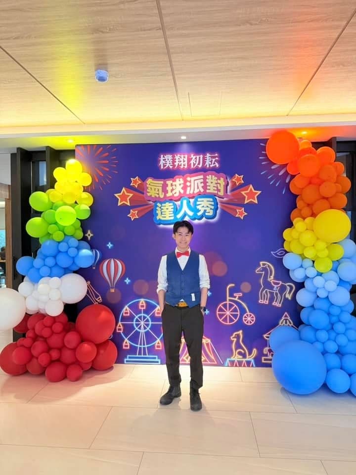 桃園中壢建案接待中心的氣球派對達人秀背板，左右兩側是彩虹色氣球柱，柯男站在中間