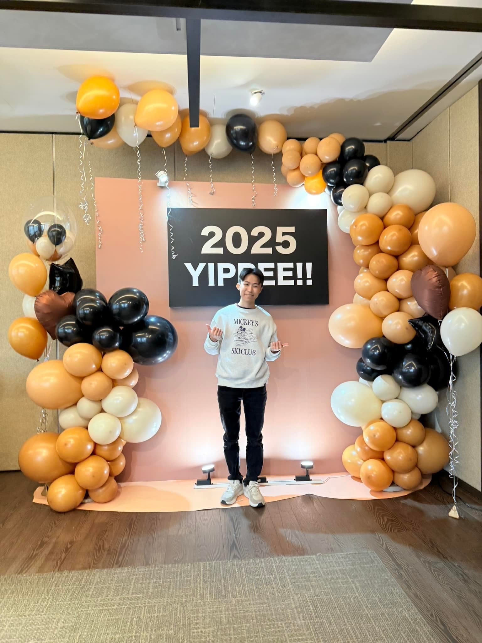 2 月春酒場：柯男站在 2025 YIPPEE 拍照牆前，前方有地燈