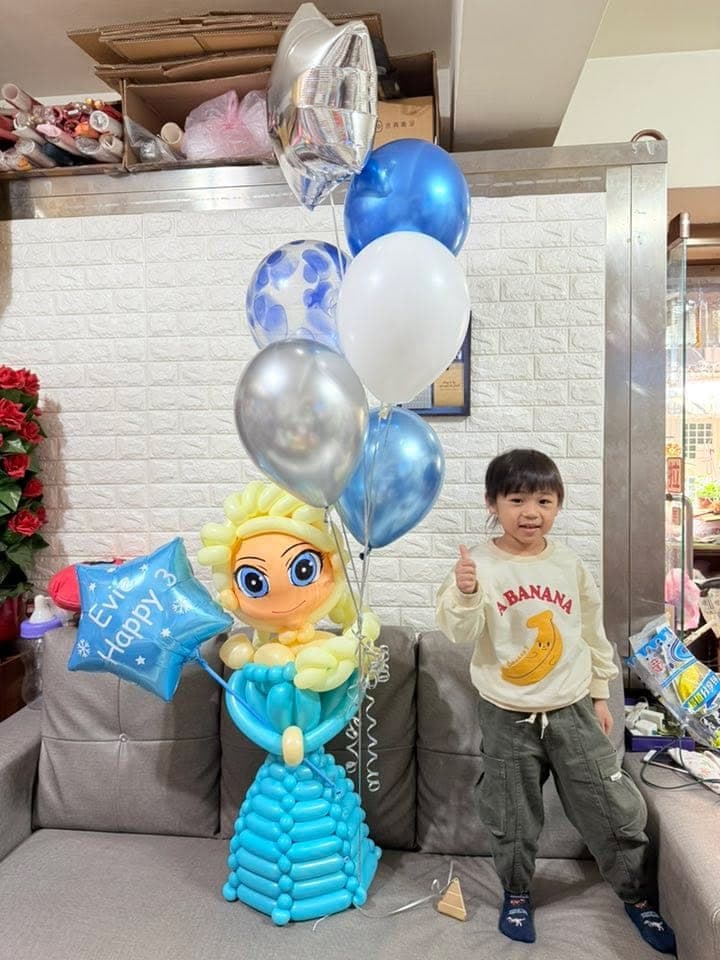 小男孩站在沙發旁比讚，身邊是艾莎氣球人偶和一大束藍色、銀色、白色空飄氣球