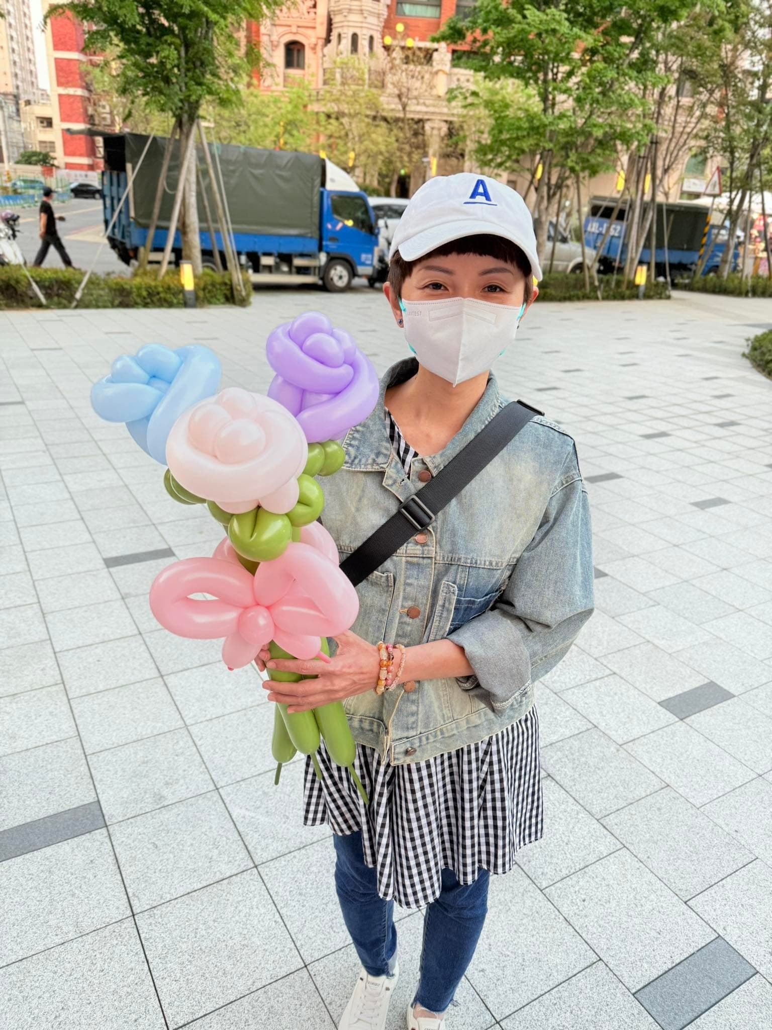 戴白色棒球帽的女士拿著藍、粉、紫色玫瑰與粉紅蝴蝶結的粉彩氣球花束