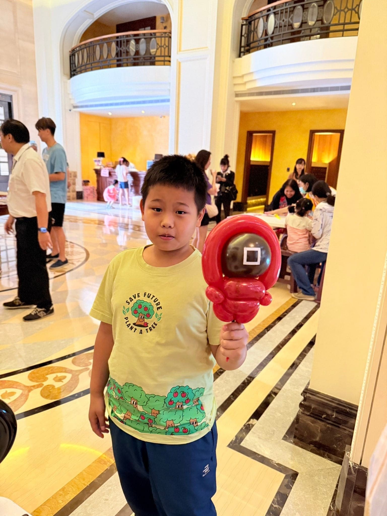 大廳折氣球那場：男孩舉著魷魚遊戲守衛造型氣球