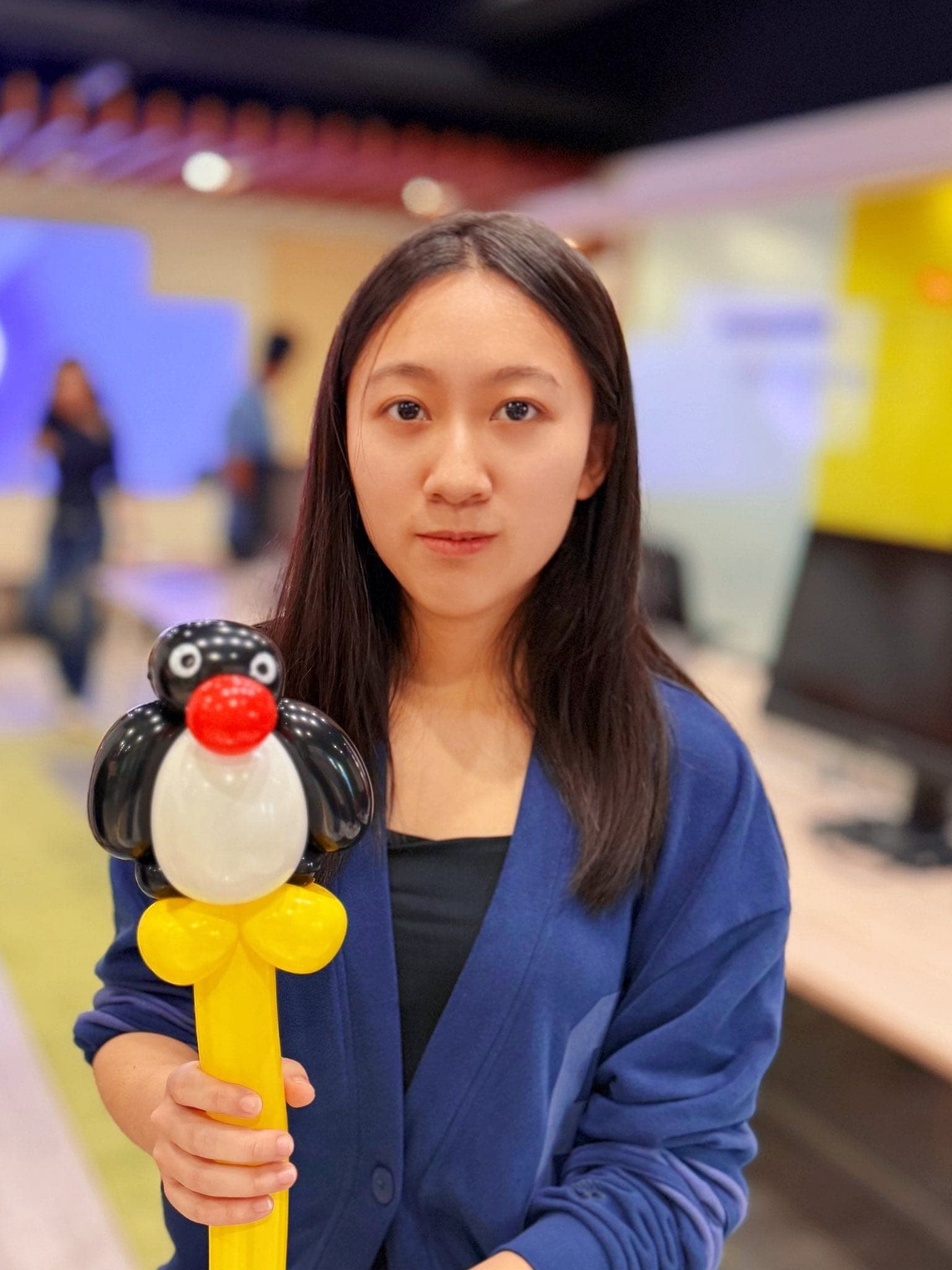 穿藍色外套的女生拿著黑白身體、紅色嘴巴的企鵝家族 Pingu 造型氣球棒