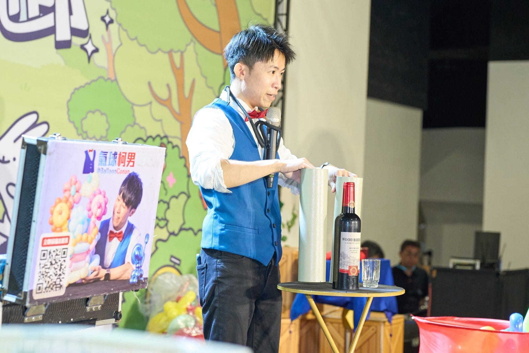 柯男在舞台小桌前表演紅酒瓶魔術