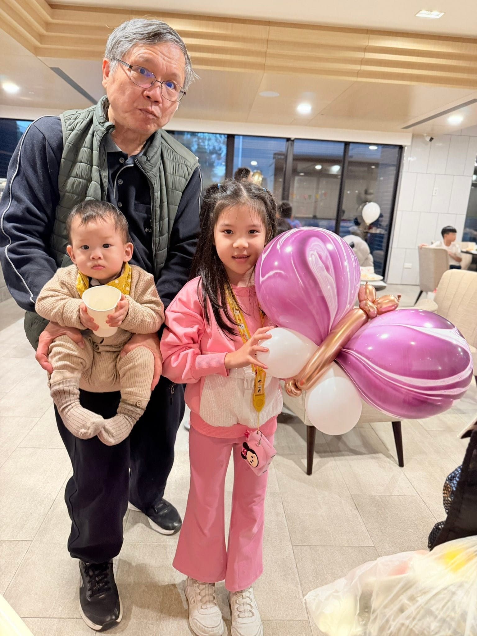 12 月抓周：粉紅外套女孩拿紫白色大蝴蝶造型氣球