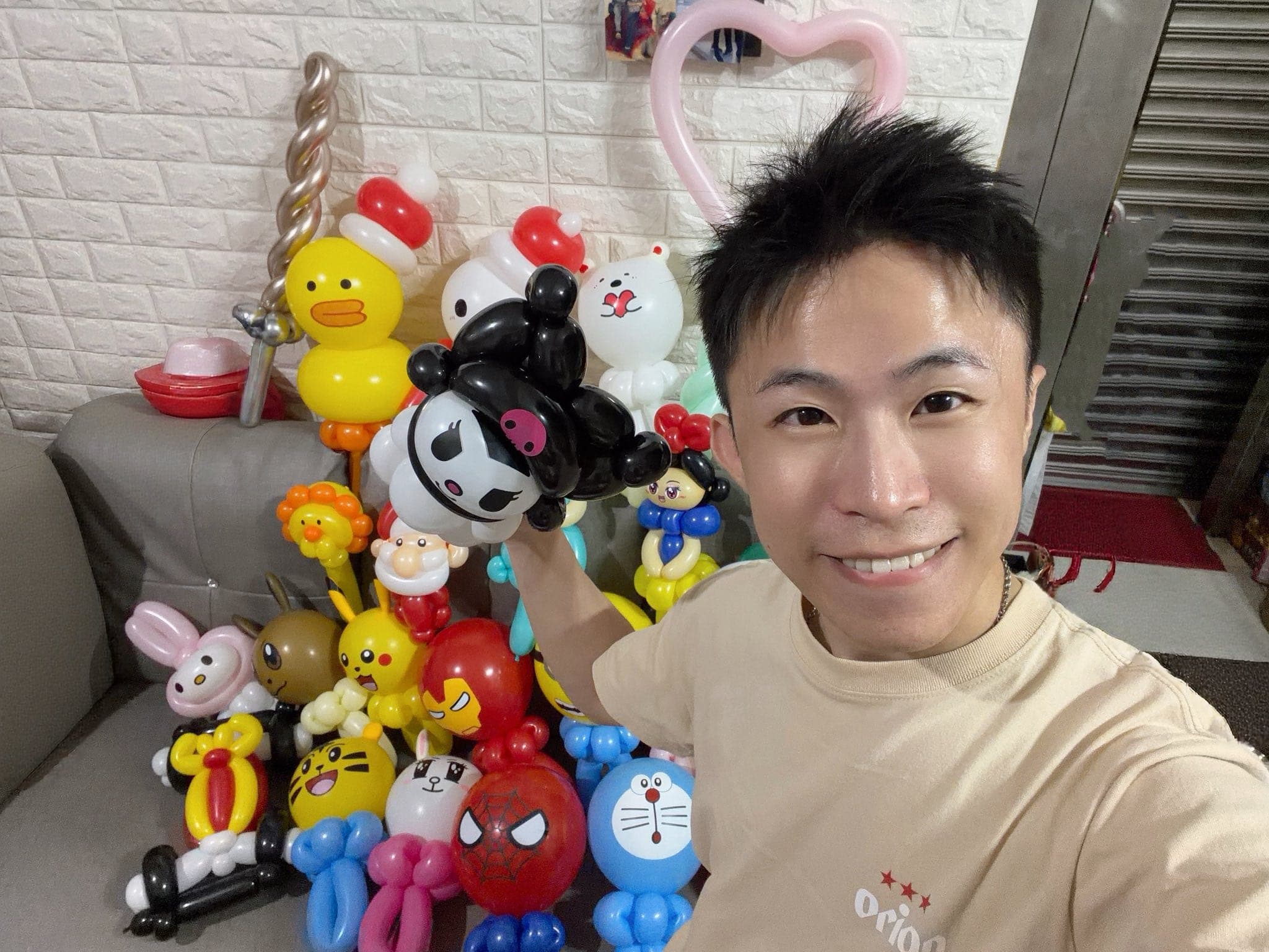 柯男拿著酷洛米造型氣球自拍，身後沙發上堆滿聖誕老公公、蜘蛛人、哆啦A夢等造型氣球