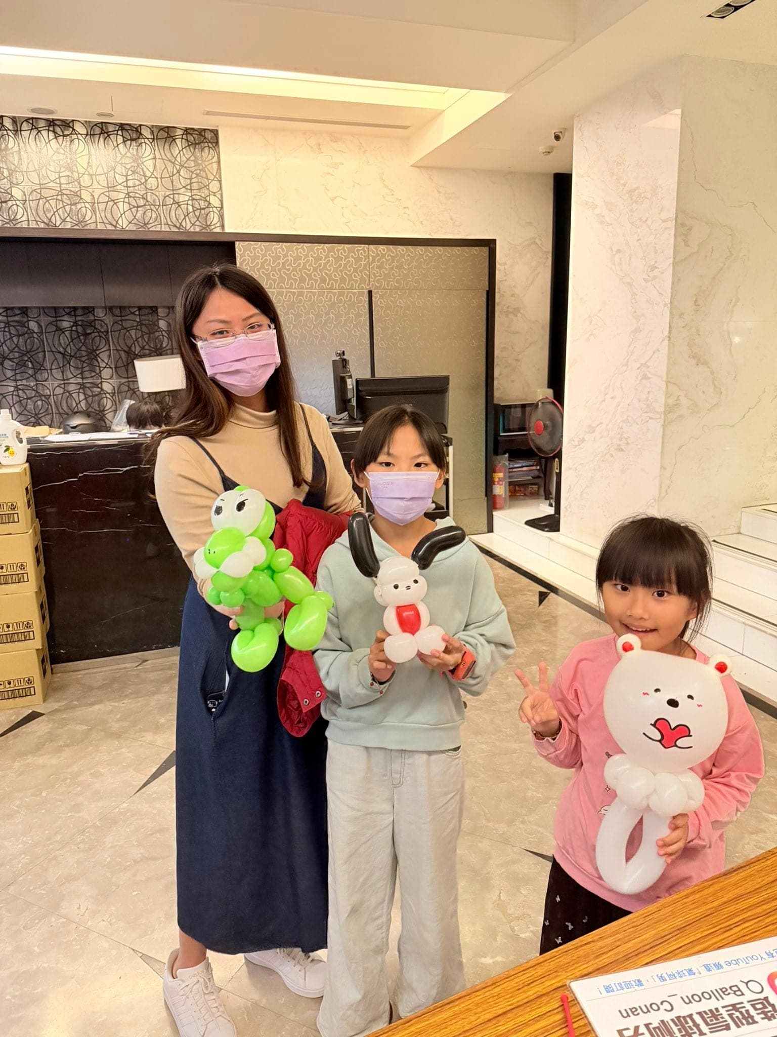 媽媽拿著綠色青蛙造型氣球，兩個女孩分別拿著白色小熊與帕恰狗造型氣球