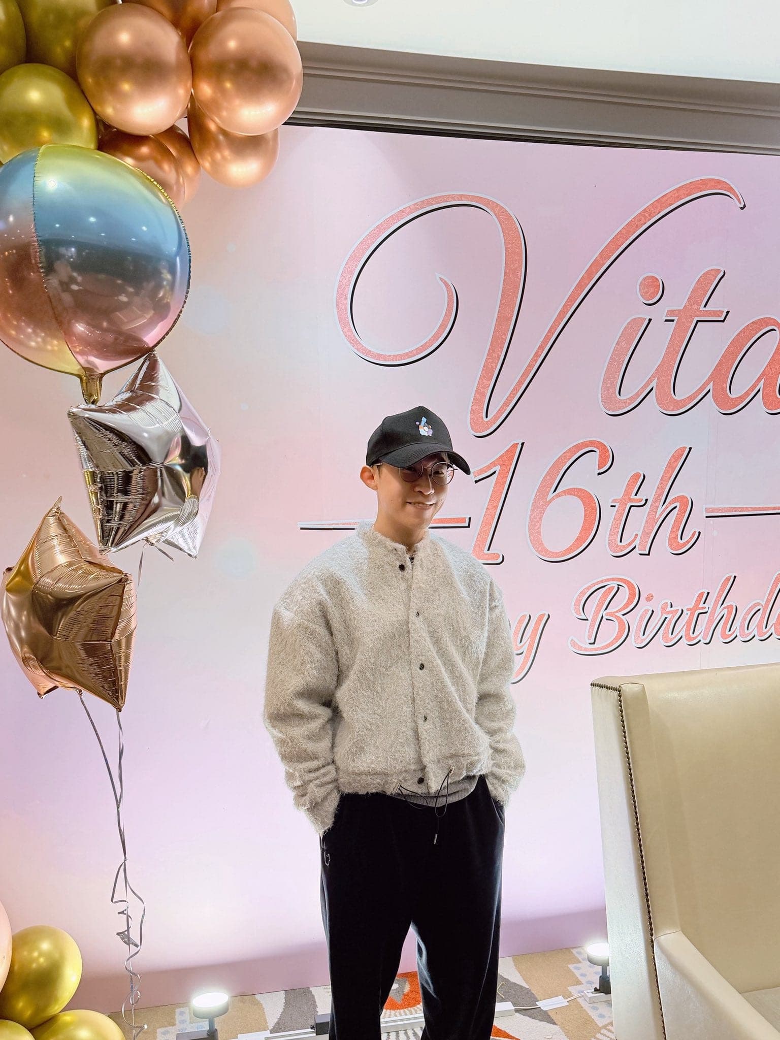 柯男戴黑色棒球帽站在粉色 16th 生日背板前，左側是玫瑰金與彩虹鋁箔氣球