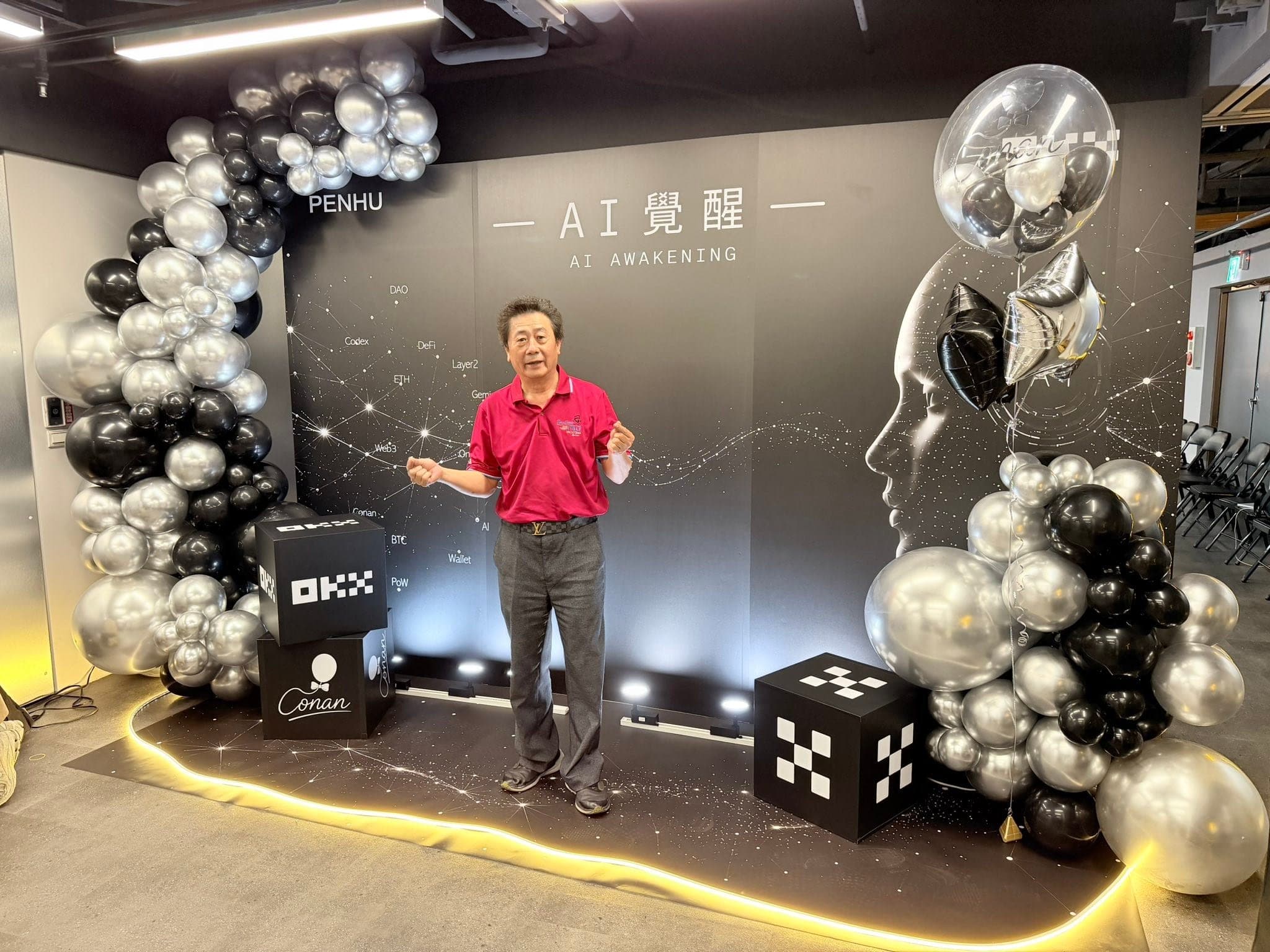 穿紅色上衣的柯爹站在 AI 覺醒背板前張開雙手，兩側黑銀氣球拱與黑色方塊道具