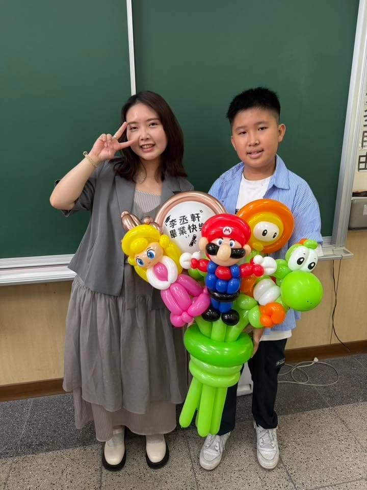 穿藍色襯衫的國小畢業生和女士在黑板前合照，畢業生抱著瑪利歐、耀西造型氣球花束