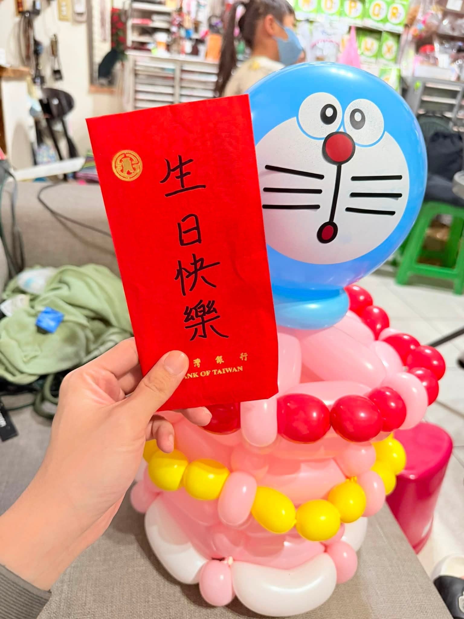哆啦A夢造型氣球前拿著寫有生日快樂的紅包