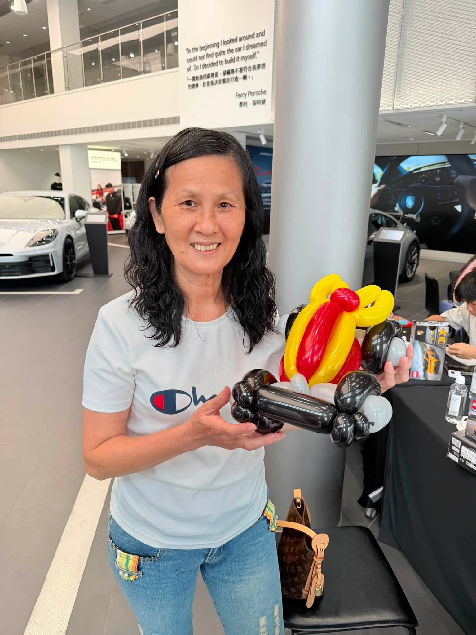 穿白色 T 恤的女士在保時捷展間拿著紅黃黑三色 F1 賽車造型氣球