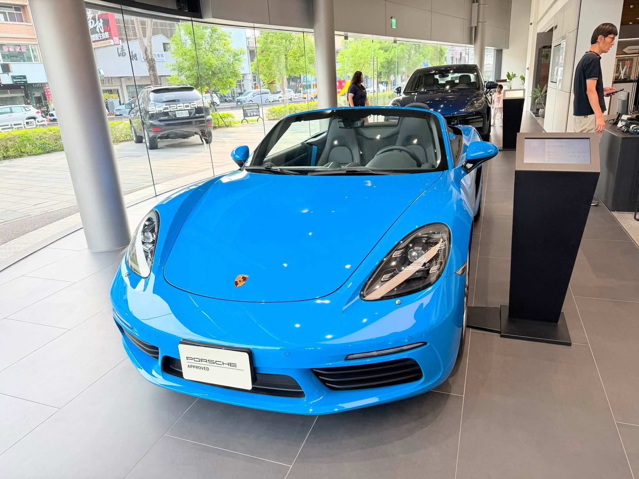 保時捷展示中心內一台天藍色敞篷跑車，車頭掛著 PORSCHE APPROVED 牌