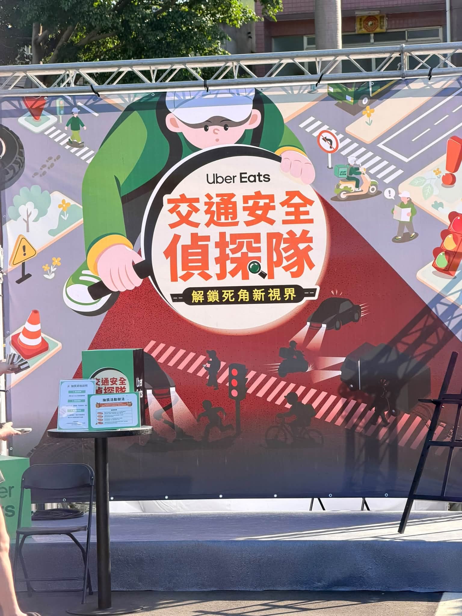 Uber Eats 交通安全偵探隊活動舞台背板，插畫是拿著放大鏡的外送員與街道