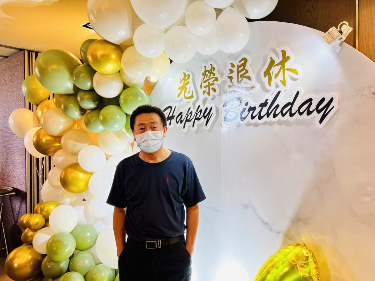 穿深藍上衣的男士站在橄欖綠金白氣球拱與大理石背板前